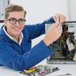 Réparateur informatique souriant en blouse bleue, travaillant sur la carte mère d'une unité centrale.