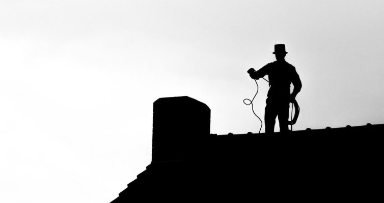 Silhouette d'un ramoneur sur toit, chapeau haut, corde à la main