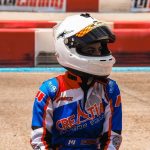 Un coureur en combinaison bleue et casque blanc sur piste terre