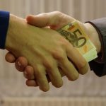 Homme en costume et homme en pull serrant la main avec des billets de 50 euros