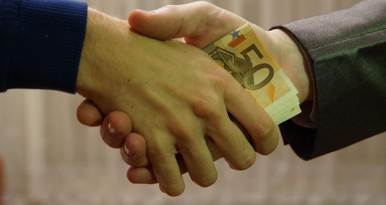 Homme en costume et homme en pull serrant la main avec des billets de 50 euros