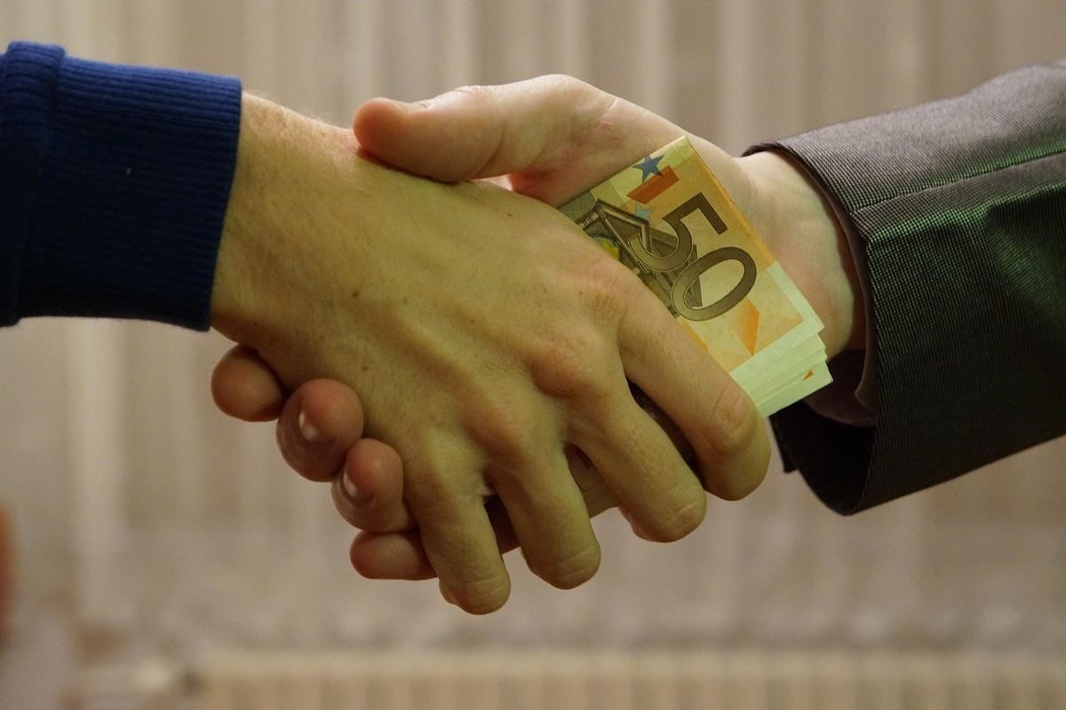 Homme en costume et homme en pull serrant la main avec des billets de 50 euros