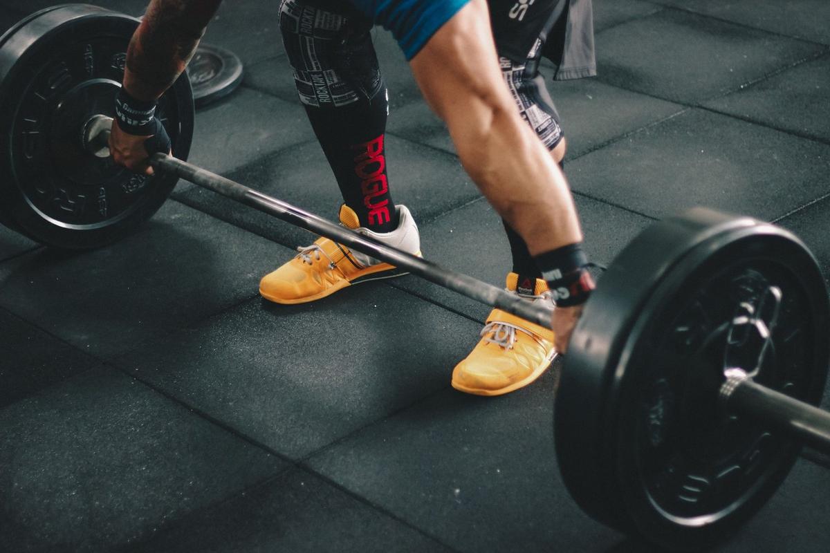 Homme musclé soulevant barre de haltères sur tapis de sol en salle de musculation